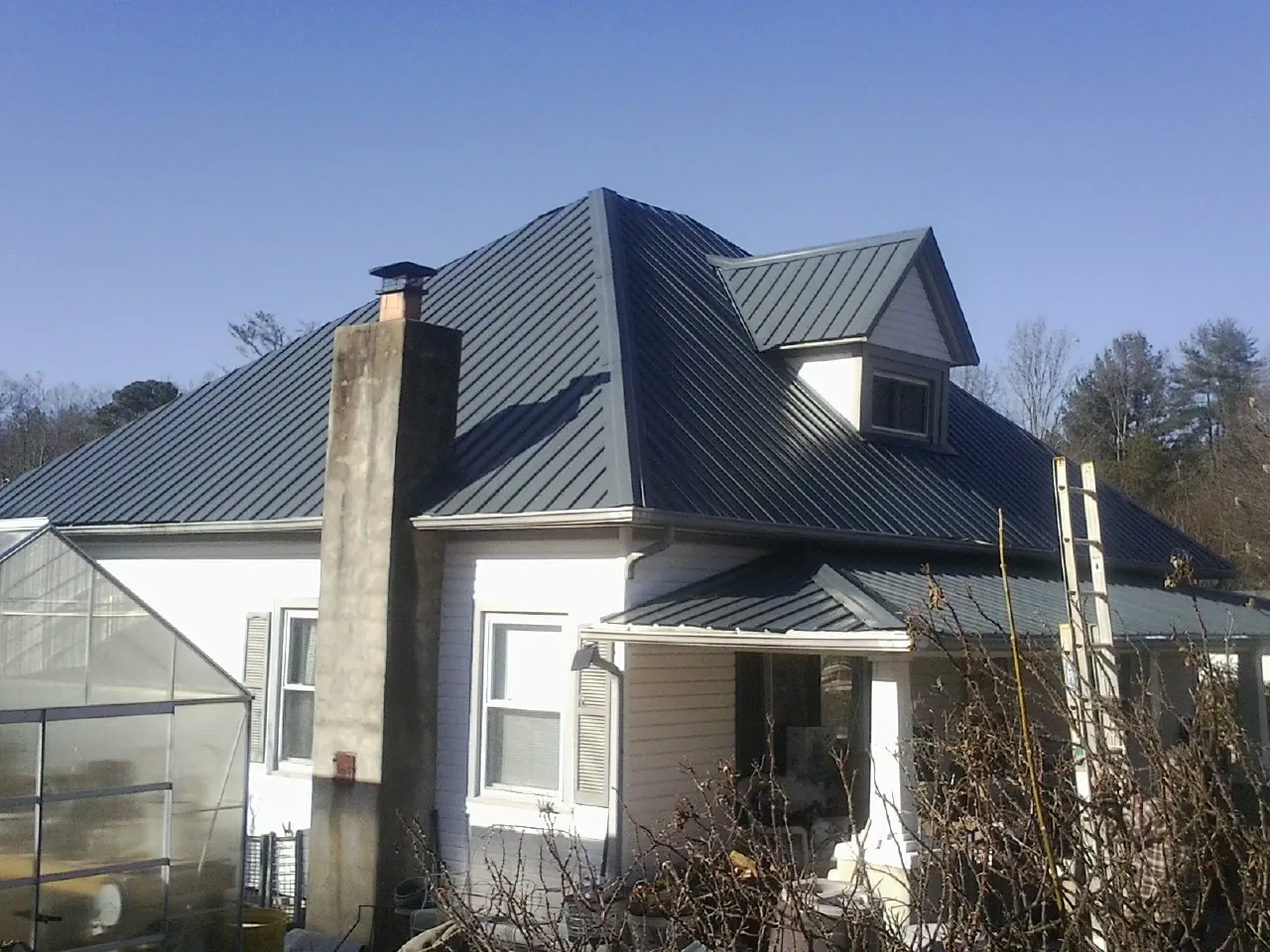 Dark blue standing seam metal roof on a white farmhouse with dormer — Slate & Tile Roof Repair by Roofing Brothers in Lunenburg