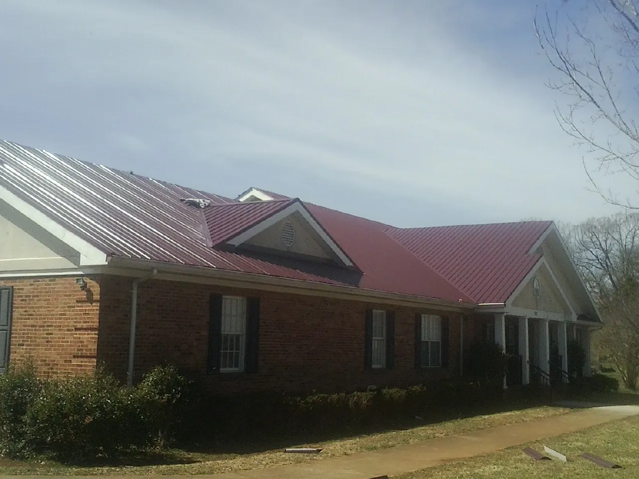Red metal roof with gabled entries on a long brick building, from a Hail Damage Roof Repair job in Lunenburg