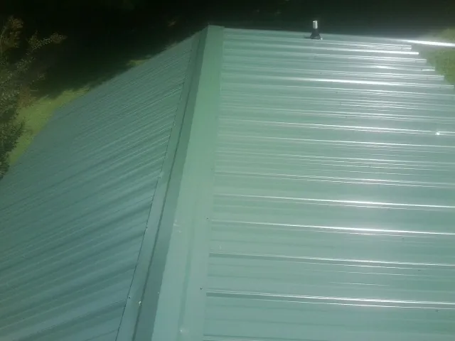 New green metal panels meeting at the ridge of a roof — Flat Roof Repair work by our crew in Lunenburg